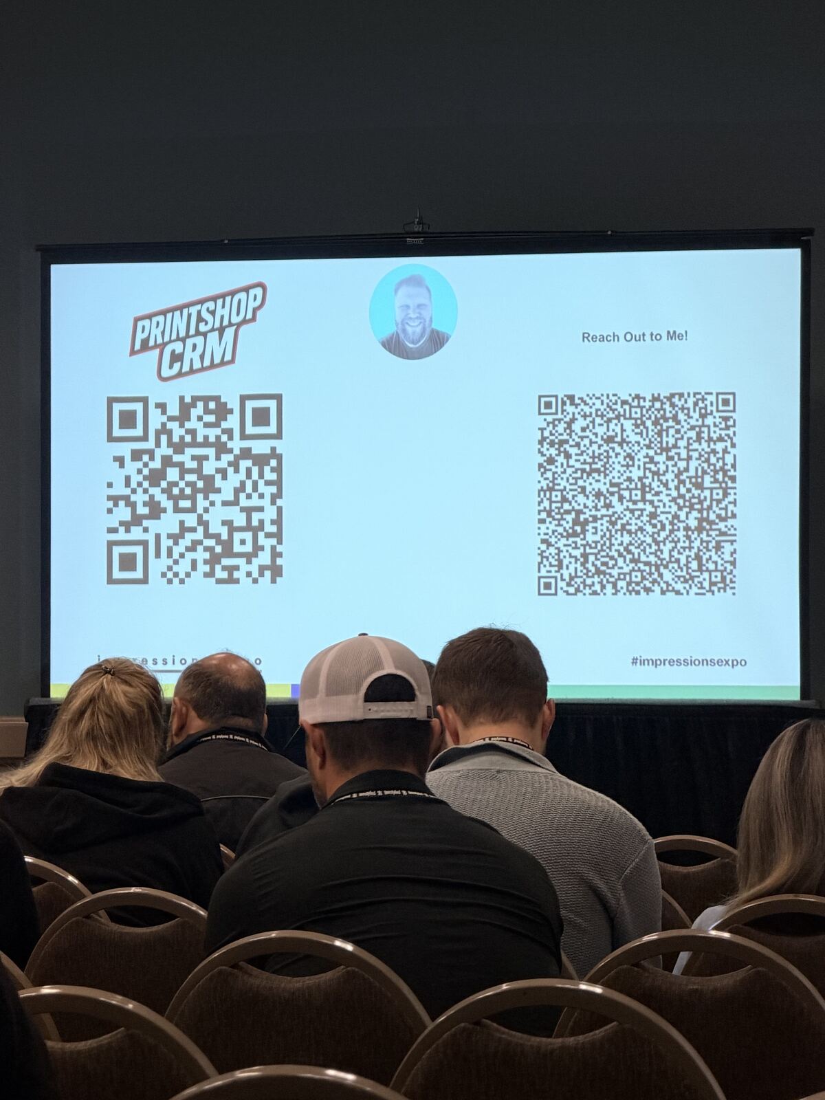 Attendees viewing a QR code display on screen at the printing booth with decorated hats visible